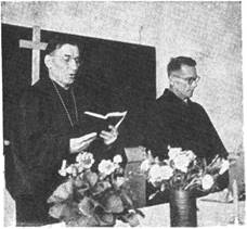 Єпископ В. Кузів читає Святе Письмо під час богослужения в українському скитальчому таборі в Регенсбургу, Ні­меччина. Світлину зроблено 21 вересня 1947 року. Поруч його стоїть д-р М. Костів.