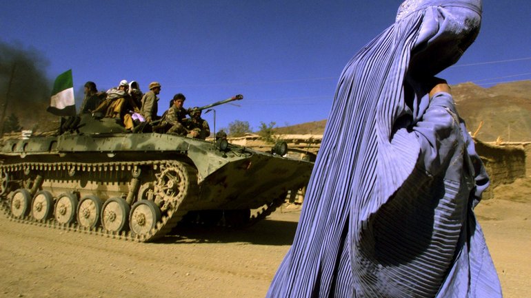 Афганка, одягнена в традиційну бурку, йде узбіччям дороги, тоді як БМП Північного альянсу (об'єднання польових командирів північного Афганістану, що боролися з талібами) їде на нову позицію на околиці міста Джабаль-Уссарадж, в 60 км на північ від Кабула, 4 листопада 2001 року. - фото 1