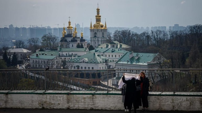 A woman puts on her headscarf in the courtyard of the Kyiv-Pechersk Lavra, also known as the Kyiv Monastery of the Caves, in Kyiv in April 2023. - фото 1