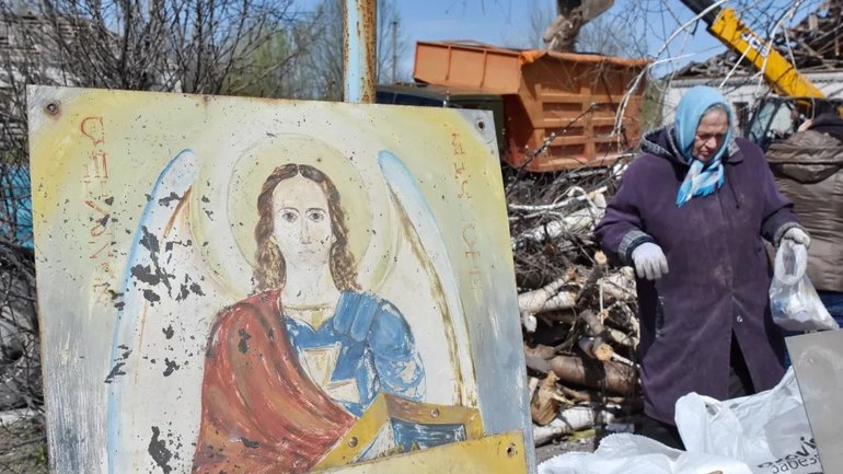 A woman walks next to a portrait of Christ as she collects what remains after a Russian rocket destroyed an Orthodox church on Easter night in Komyshuvakha in 2023. - фото 1