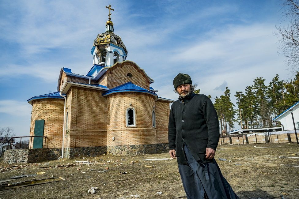 Priest Romanov of Yasnohorodka stands in front of his church after it was hit by shelling - фото 90767