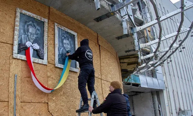 Ukrainian artist Gamlet Zinkovsky (top) sets up two paintings by Polish artist Maciej Vogel on the wall of a building in Kharkiv. The paintings depict two women knitting a scarf in the colours of the Ukrainian and Polish national flags. - фото 105126