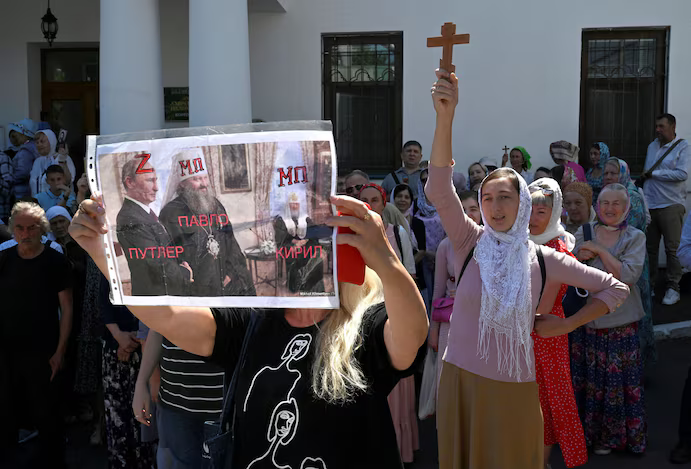 A woman outside the Kyiv-Pechersk Lavra monastery in July 2023 holds a photo of Russian President Vladimir Putin awarding the Order of Friendship medal to UOC priest Metropolitan Pavlo, head of the monastery, in 2013. - фото 139741